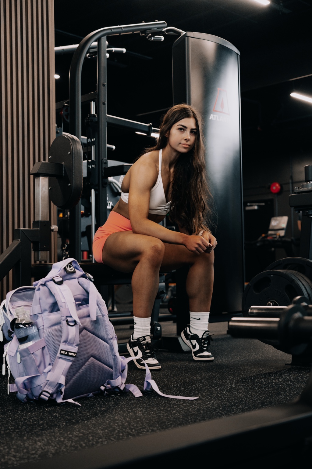 Maddie Warren seated in a gym wearing a white sports bra and orange shorts